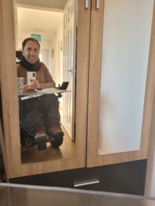 Martyn taking a selfie in his wardrobe mirror wearing a brown jumper, dark grey joggers and light grey shoes