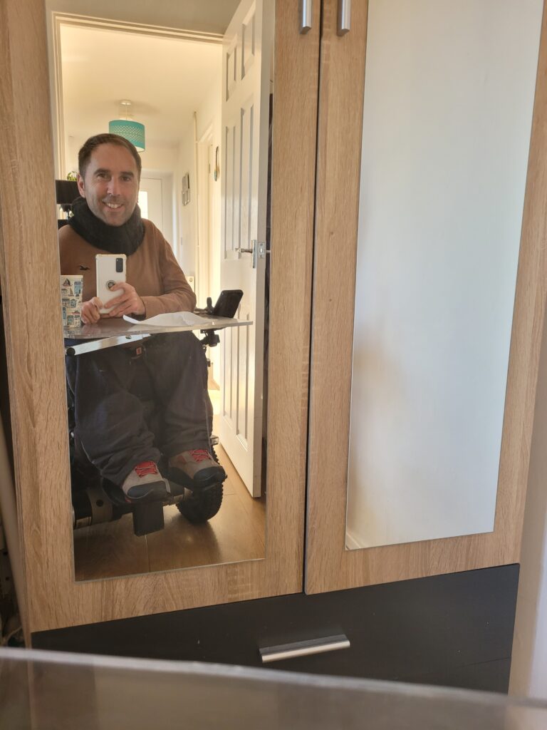 Martyn taking a selfie in his wardrobe mirror wearing a brown jumper, dark grey joggers and light grey shoes