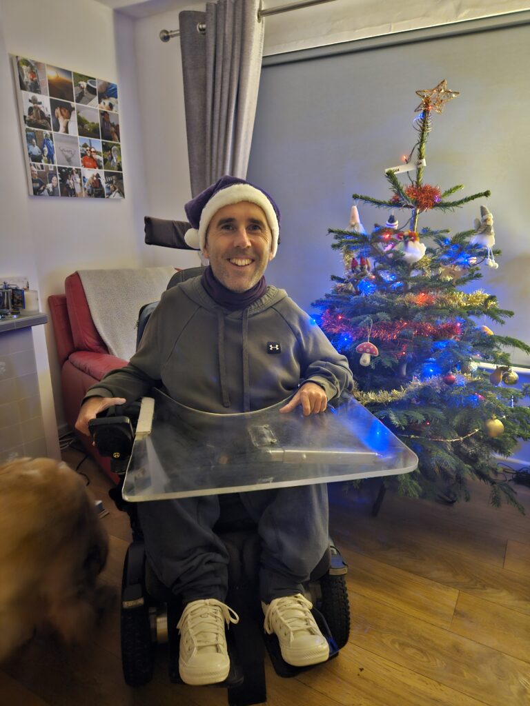 Martyn in his purple Christmas hat next to the Christmas tree posing for the year end post about 2023