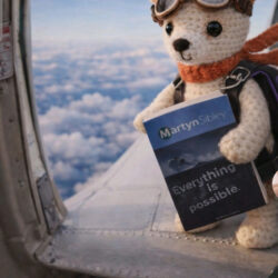 A small knitted dog mascot wearing aviator goggles and a scarf sits on the edge of an aeroplane door high above the clouds, holding the book Everything is Possible by Martyn Sibley, creating a playful, adventurous travel scene.
